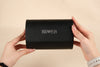 Black wallet held by hands with 'BS❤️EB' branding on a beige background