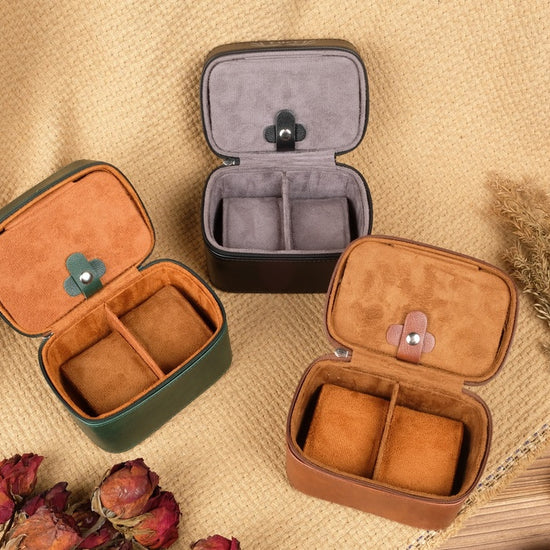Three open jewelry cases on a textured surface with dried flowers and pinecones.
